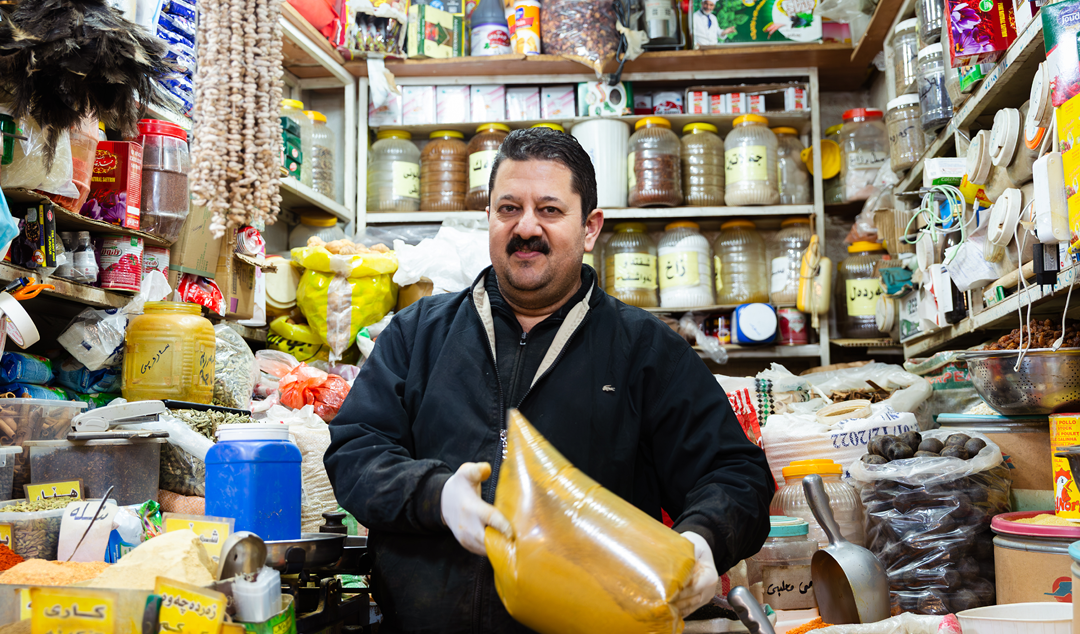 smiling man holding a bag of sauce in a Middle Eastern market