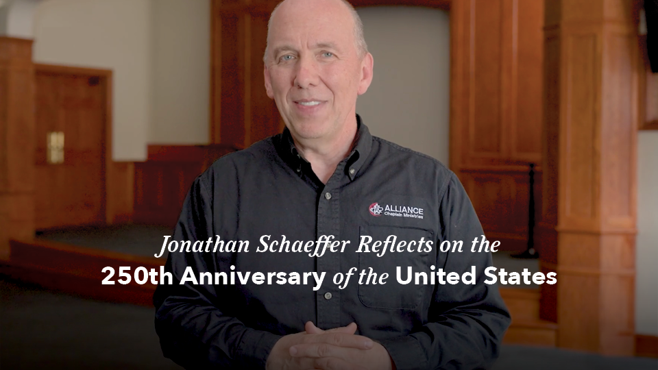 Video thumbnail showing a person standing indoors in front of wood-paneled architectural features, wearing a dark button-down shirt with the Alliance Chaplain Ministries logo. Overlay text reads: “Jonathan Schaeffer Reflects on the 250th Anniversary of the United States”
