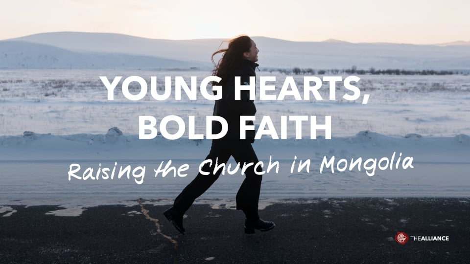 A woman is walking along a paved road through a snowy, open landscape with distant hills. Overlaid text reads, “Young Hearts, Bold Faith. Raising the Church in Mongolia.” An Alliance logo appears in the bottom right corner.