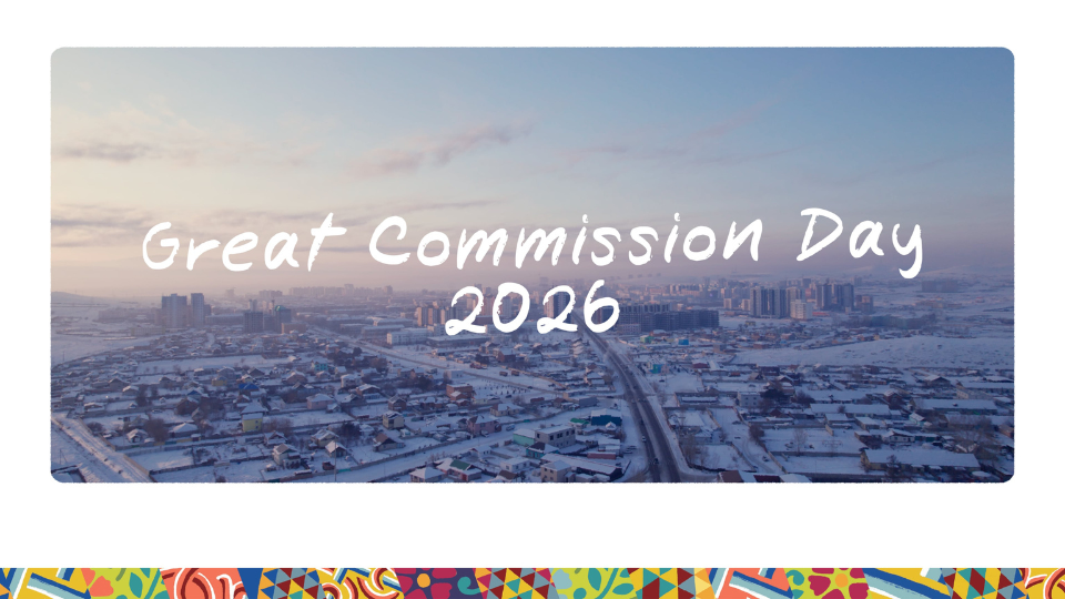 A wide aerial view of a snowy cityscape at sunrise or sunset, with roads and buildings stretching into the distance. Over the image, white handwritten-style text reads ‘Great Commission Day 2026.’ A colorful patterned border decorates the bottom of the design.