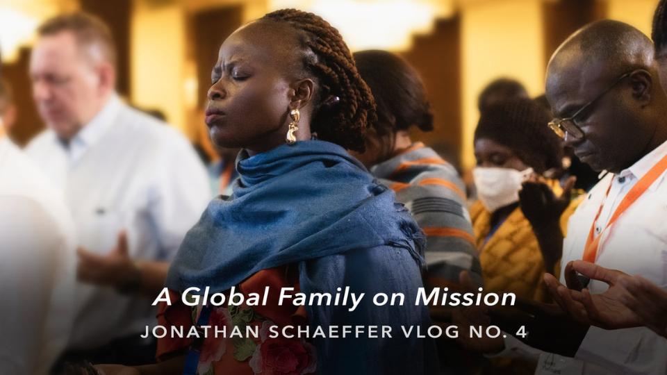 People gathered indoors, worshiping together, with text overlay reading “A Global Family on Mission – Jonathan Schaeffer Vlog No. 4.”