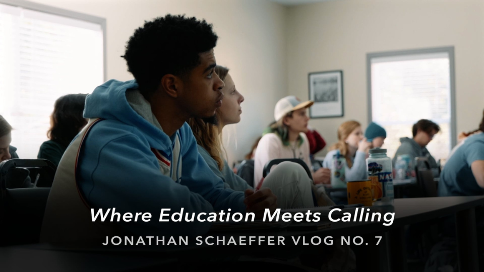 A classroom of students seated at desks, listening attentively to someone out of frame. Sunlight comes through windows on the right side of the room. Text over the image reads “Where Education Meets Calling – Jonathan Schaeffer Vlog No. 7.”