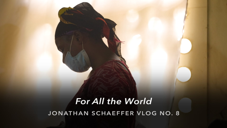 A silhouetted person wearing a face mask and patterned head covering stands in profile against a softly lit background with circular light bulbs. Text over the image reads “For All the World” and “Jonathan Schaeffer Vlog No. 8.”
