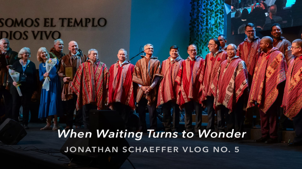 Group on stage wearing red and beige with Spanish text on backdrop. Overlay reads “When Waiting Turns to Wonder – Jonathan Schaeffer Vlog No. 5.”